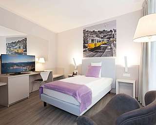 Ein helles Hotelzimmer mit Einzelbett, Schreibtisch und Fernseher.